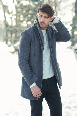 outdoor portrait of young handsome man in warm coat walking alone in snowy parkの写真素材