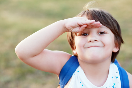 smiling little boy salutes or covering his face from sun with his handの写真素材