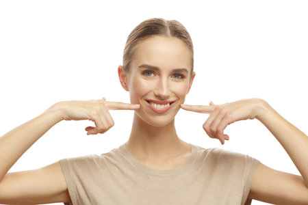 Portrait of beautiful woman smiling pointing to her white and healthy teeth isolated over white...