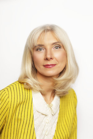 Beautiful blond lady in her 50s wearing yellow jacket posing over white background