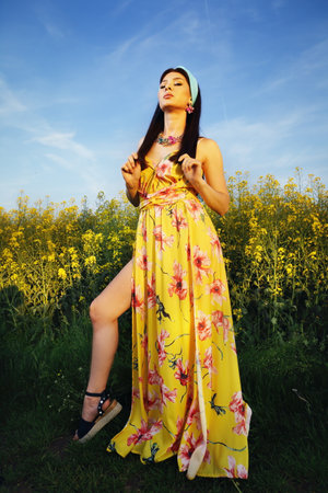 Beautiful fashion woman posing on field with yellow flowers in yellow dressの写真素材
