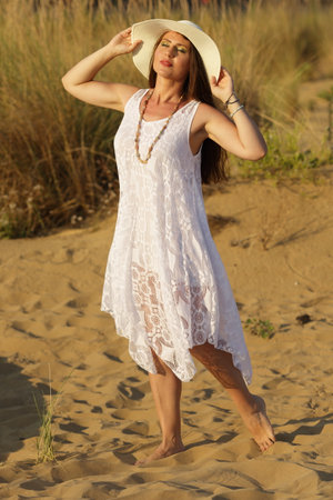 beautiful woman in hat sitting on the beach in sand and dunes fashion photoの写真素材