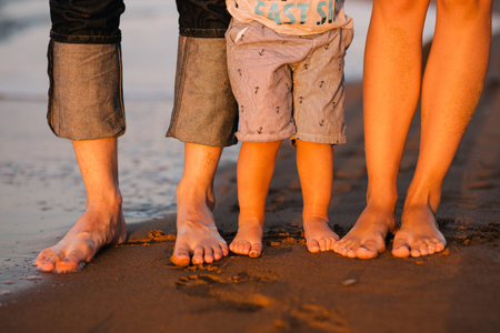 feet of a young family on a sea beach. Feet of mother, the father and the child stand on sand at...