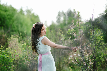 The girl in a blue dress poses against the green woodの写真素材