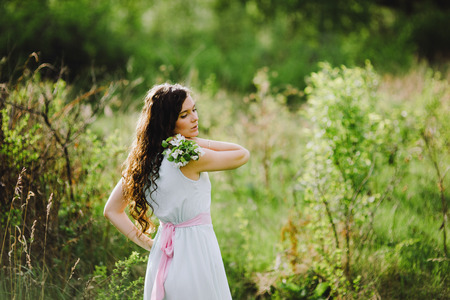 the girl with a bouquet of white flowers in a blue dress with a pink belt poses in the woodの写真素材