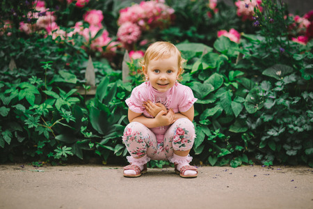 the little girl with white hair and blue eyes in a pink t-shirt poses against flowersの写真素材