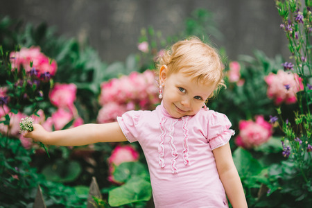 the little girl with white hair and blue eyes in a pink t-shirt poses against flowersの写真素材