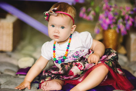 the child in a multi-colored dress with a beads sits on stonesの写真素材