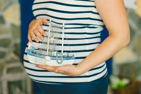toy ship in hands at the pregnant woman in a stripped vestの写真素材