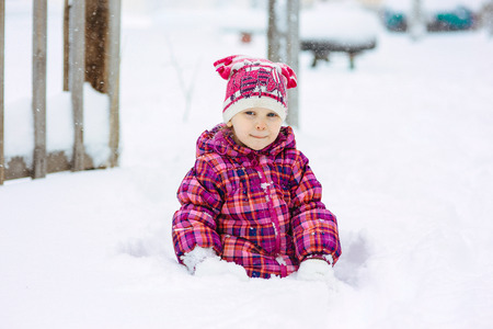 the girl in a lilac down-padded coat walks in snow weather on snowdriftsの写真素材