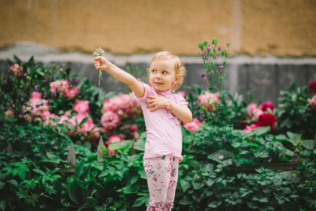 the little girl with white hair and blue eyes in a pink t-shirt poses against flowersの写真素材