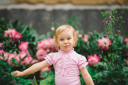 the little girl with white hair and blue eyes in a pink t-shirt poses against flowersの写真素材