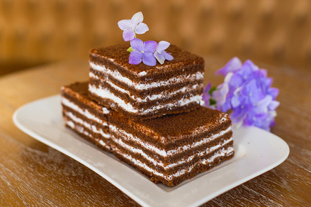 chocolate cakes on a white plate which costs on a table, lie flowers nearbyの写真素材