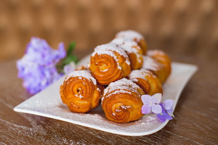 cream cake on a white plate which costs on a table, flowers lie nearbyの写真素材