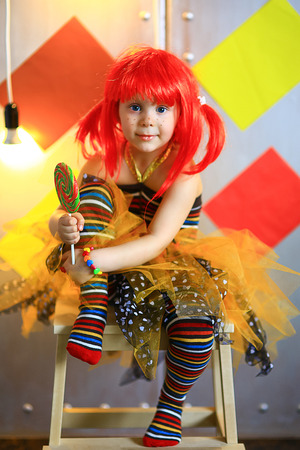 the small the girl in a red wig with freckles poses on the camera with lollipop in striped stockingsの写真素材