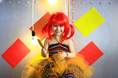 the small the girl in a red wig with freckles poses on the camera with lollipop in striped stockingsの写真素材