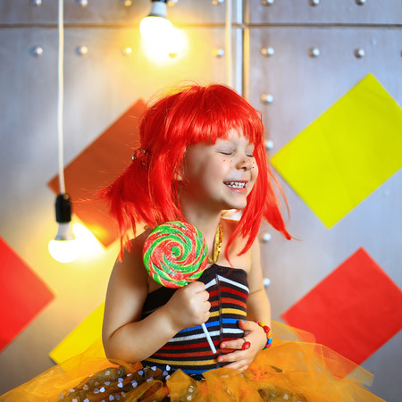 the small the girl in a red wig with freckles poses on the camera with lollipopの写真素材