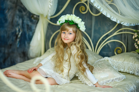 the girl with a wreath from white roses and white hair poses on the forged bedの写真素材