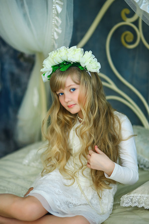 the girl with a wreath from white roses and white hair poses on the forged bedの写真素材