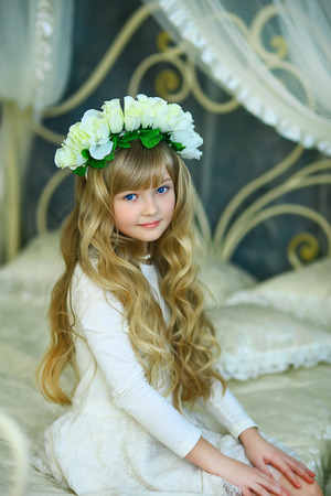 the girl with a wreath from white roses and white hair poses on the forged bedの写真素材