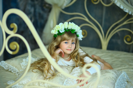 the girl with a wreath from white roses and white hair poses on the forged bedの写真素材