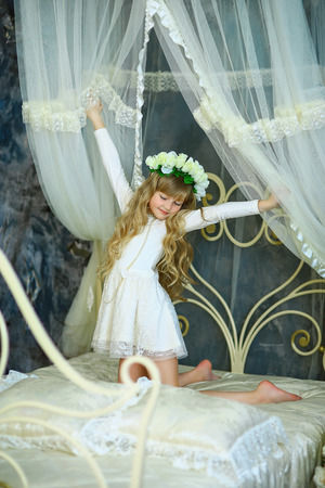 the girl with a wreath from white roses and white hair poses on the forged bedの写真素材