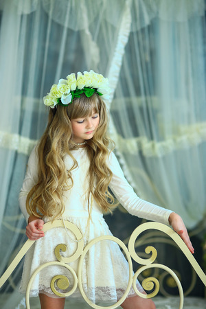 the girl with a wreath from white roses and white hair poses on the forged bedの写真素材