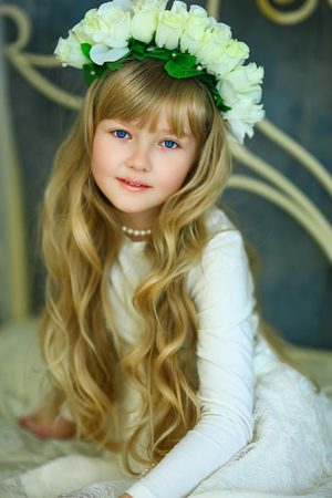 the girl with a wreath from white roses and white hair poses on the forged bedの写真素材