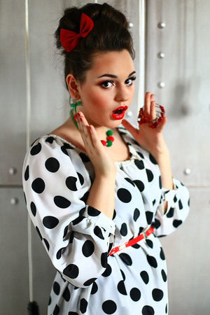 the girl in a white dress in black peas with red lipstick poses against a metal wall with bulbsの写真素材