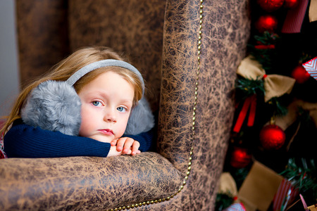 the girl in gray fur earphones sits in a chair near a Christmas fir-treeの写真素材