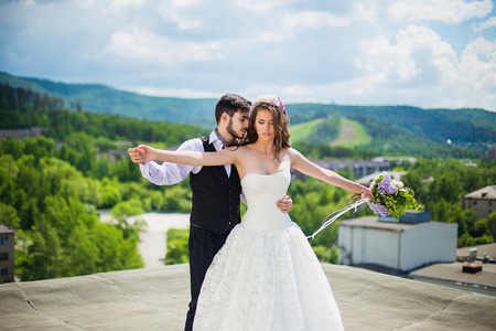 the groom with the bride stand in an embrace on the rooftop. In a hand at the bride a lilac bouquetの写真素材