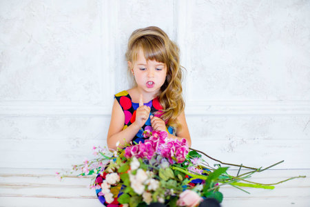 the little girl poses near flowers a multi-colored dress with a smile upon the face