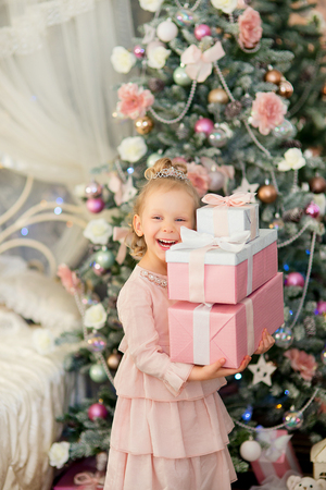 the little girl with white hair and a silver crown got up with gifts 
near a Christmas fir-tree also laughsの写真素材