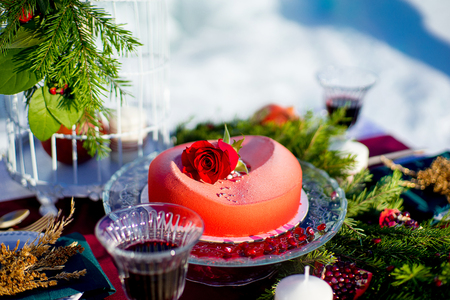red cake with a rose on a holiday table, stands a glass of red wine nearby, grains of pomegranate and pine branches lieの写真素材
