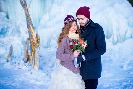 the groom with the bride pose in red caps with a bouquet of flowers in the winter against an ice floeの写真素材