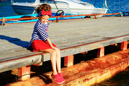 young girl sitting on the dock, laughing and smiling, looking aroundの写真素材