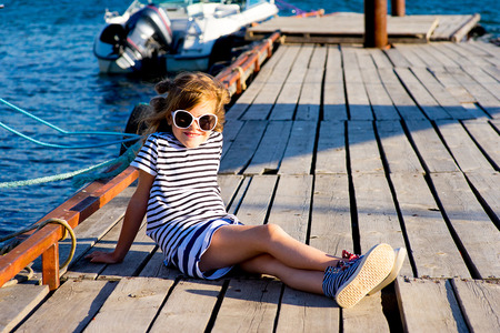 young girl sitting on the dock, laughing and smiling, looking aroundの写真素材