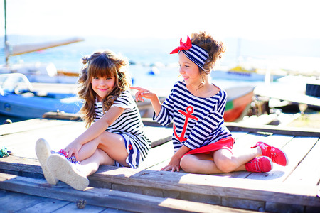 two young girls sitting on the dock, laughing and smiling, looking aroundの写真素材