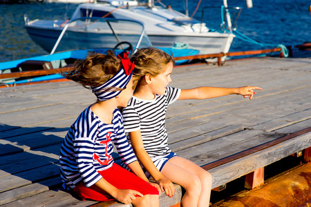 two young girls sitting on the dock, laughing and smiling, looking aroundの写真素材