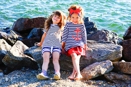 two young girls near the sea rock looking around and smilingの写真素材