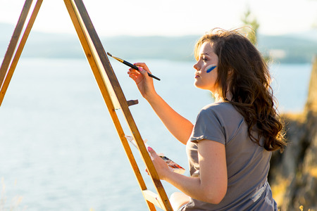young artist draws a seascape at sunset on the highrockの写真素材