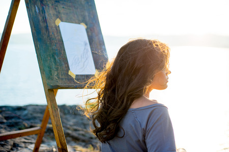 young artist draws a seascape at sunset on the highrockの写真素材