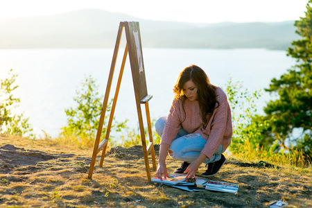 young artist draws a seascape at sunset on the highrockの写真素材