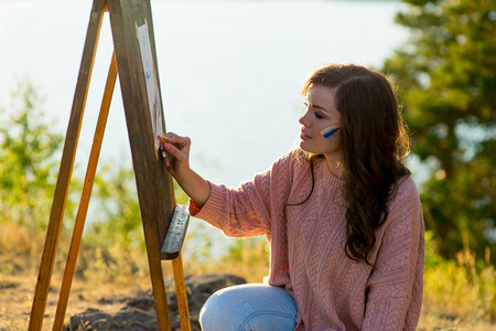 young artist draws a seascape at sunset on the highrockの写真素材
