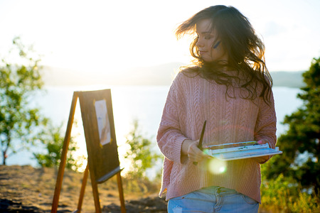 young artist draws a seascape at sunset on the highrockの写真素材