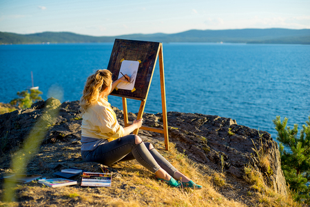 young artist draws a seascape at sunset on the highrockの写真素材