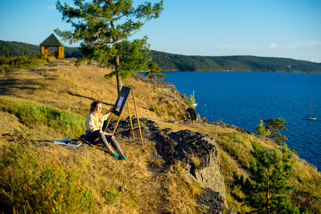 young artist draws a seascape at sunset on the highrockの写真素材