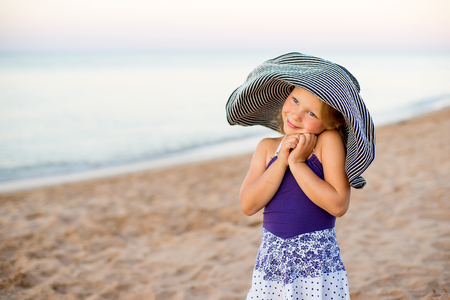 Little girl in a hat with a wide brim on the seashore posing and look aroundの写真素材