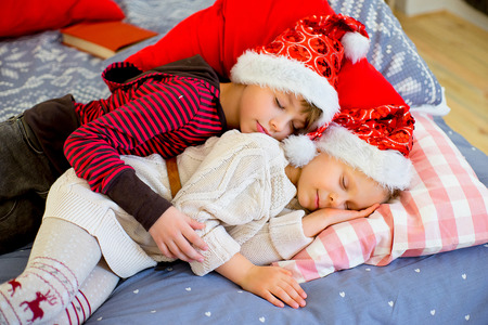 two children get sleepy till they await christmas lying on decorated bedの写真素材
