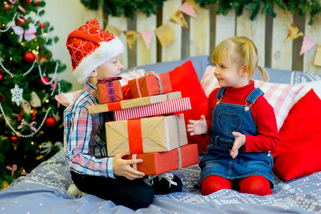 Boy and girl give gifts near a Christmas tree in red hatsの写真素材